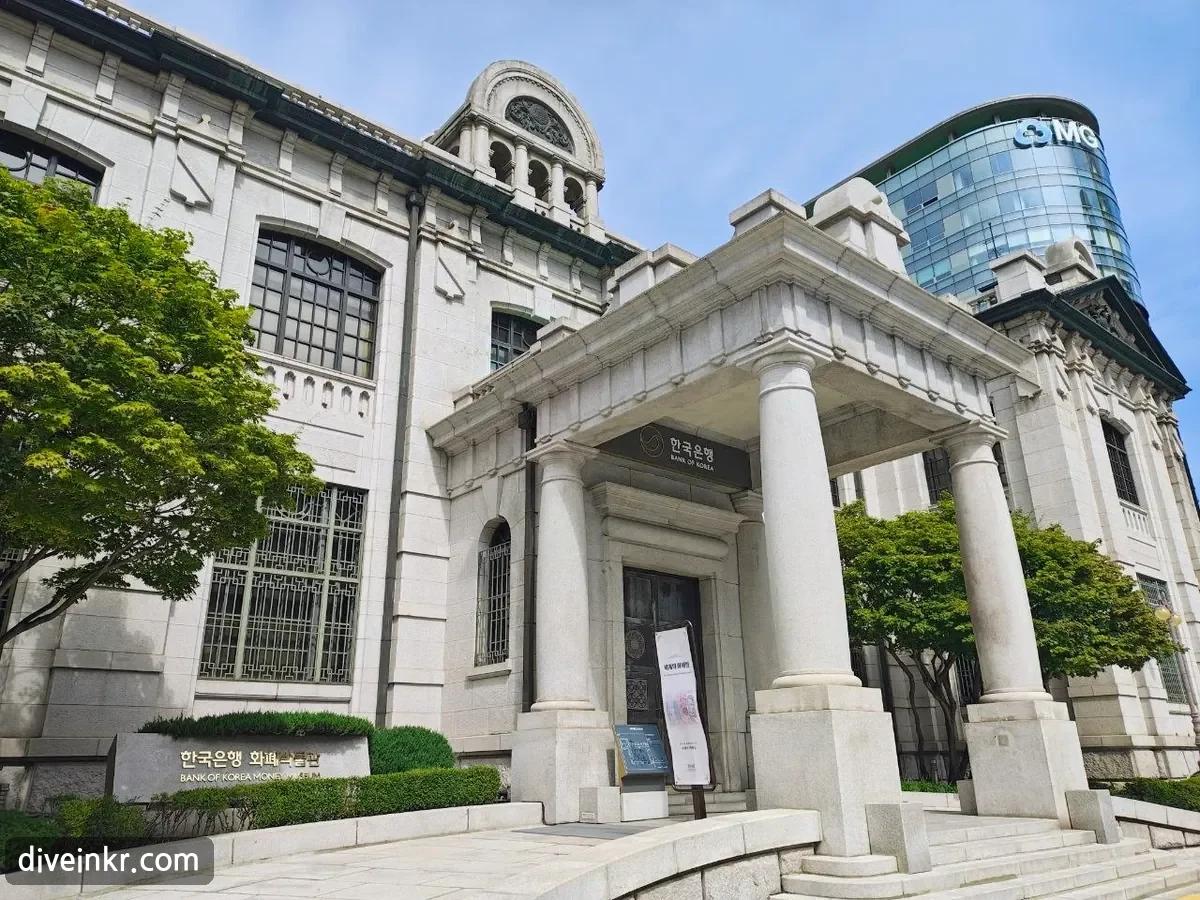 The granite Renaissance-style Bank of Korea Money Museum with a columned entrance portico, arched windows and a domed turret, a sign reading 한국은행 BANK OF KOREA over the door and a stone marker reading 한국은행 화폐박물관 BANK OF KOREA MONEY MUSEUM