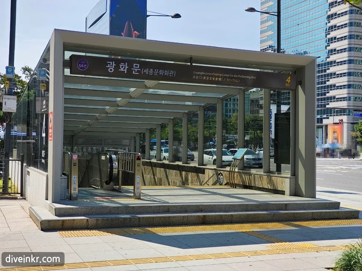 The glass-roofed entrance to exit 4 of Gwanghwamun Station on subway Line 5, with a sign reading 광화문(세종문화회관) Gwanghwamun (Sejong Center for the Performing Arts) and an escalator going down (faces blurred)