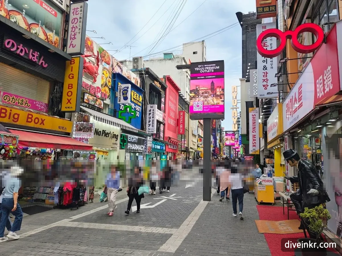 A pedestrian shopping street in Myeongdong, Seoul, with signs in Japanese (のかばん), English (BIG BOX, EIGHT PHARMACY) and Korean, a green pharmacy cross, a large red glasses-shaped sign above a shop reading 眼鏡, and shoppers walking past (faces blurred)