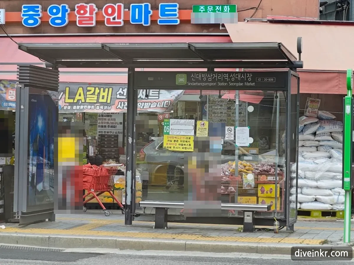 A covered Seoul bus stop with a sign showing the stop name in Korean and English and a stop ID, with route signs and a yellow notice posted on the glass