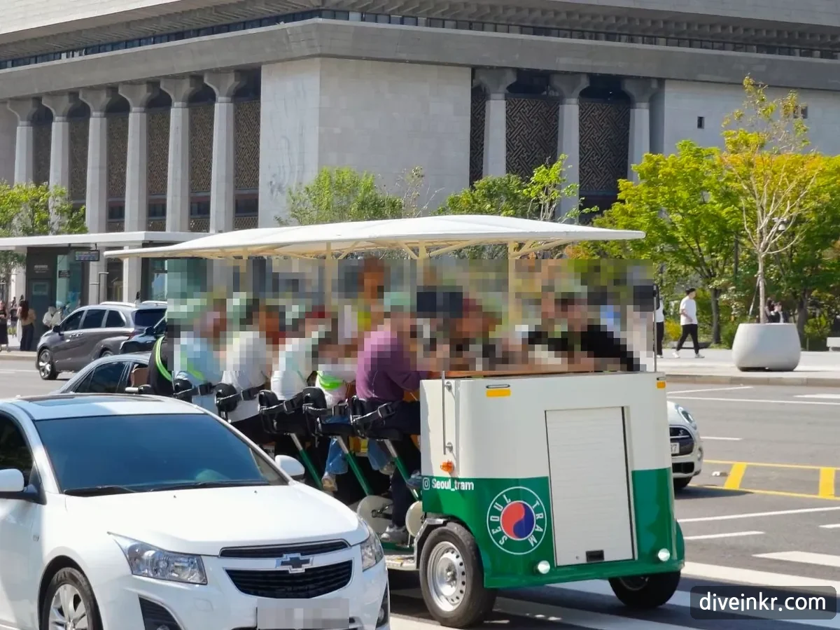 A green-and-white Seoul Tram pedal vehicle with a white canopy, carrying a group of riders who pedal together, on a road in front of the Sejong Center (faces and license plate blurred)